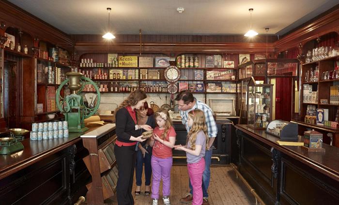 inside the shop, presented as it would have been circa 1920s. The shop is fitted out with dark wooden shelves and a dark wood counter on 3 sides of th